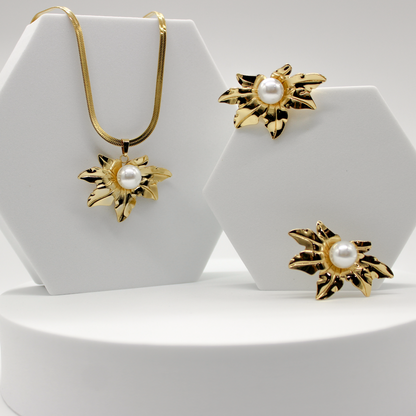 Gold jewelry set featuring a necklace and matching earrings with sunburst flower motifs and white pearl centers, displayed on white hexagonal stands.