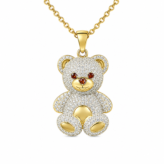 A gold-tone teddy bear pendant necklace encrusted with clear pavé stones, featuring small red gemstone eyes and a gold-tone chain, shown on a plain white background.